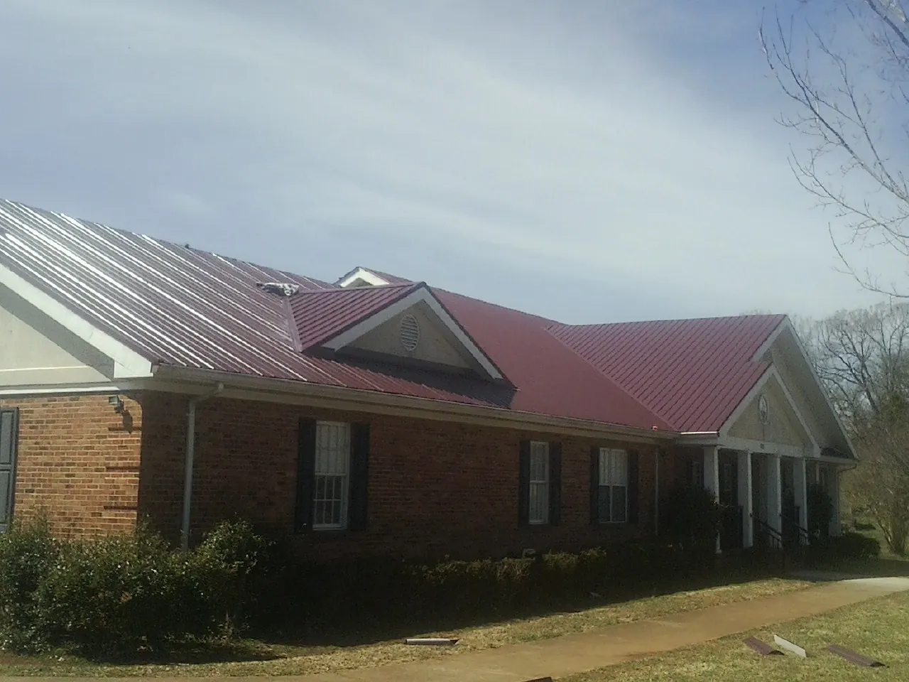 Red metal roof with gabled entries on a long brick building, from a Hail Damage Roof Repair job in Dana